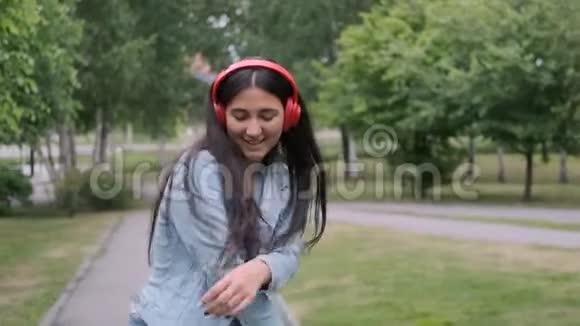 时尚活泼的女孩在公园里跳舞听着耳机上的音乐视频的预览图