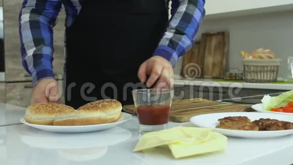 大个子在家做汉堡包丰满的男人把番茄酱涂在面包上不健康的生活方式油炸和高视频的预览图