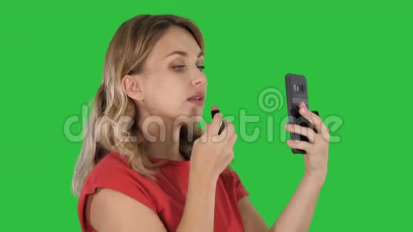 金发女人涂口红在绿色屏幕上看手机色度键视频的预览图