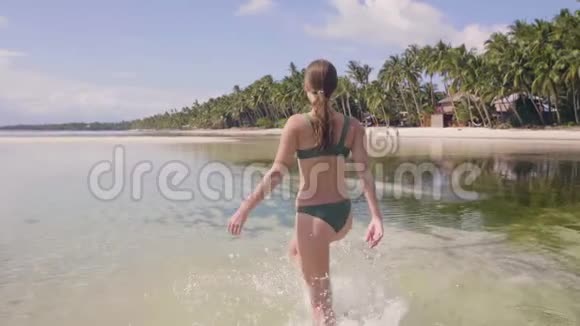 穿泳衣的年轻女子在热带海滩的透明海水上散步快乐的女人享受清澈的海水视频的预览图