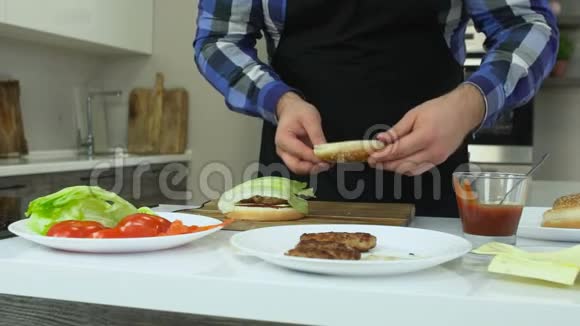 穿围裙的胖子在家做汉堡包所有的配料和产品都在桌子上不健康的生活方式油炸视频的预览图