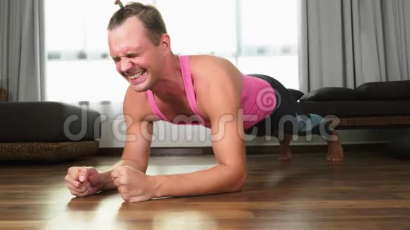 贪玩的帅哥穿着一件粉红色的t恤从事健身在他家的客厅里视频的预览图