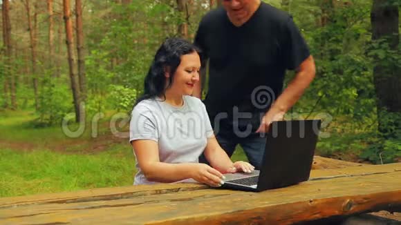 坐在长凳上的公园里的男人和女人讨论在笔记本电脑上浏览视频的预览图
