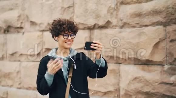 时尚的年轻女士正在网上打视频电话用智能手机说话和打手势看着屏幕穿着视频的预览图