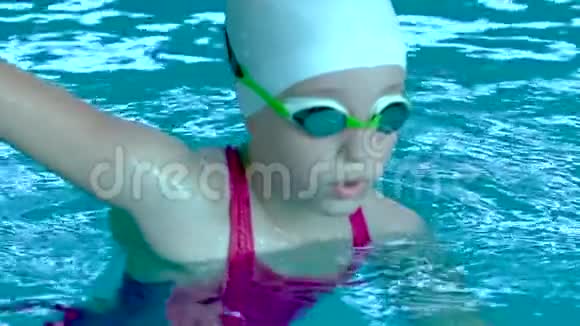 戴着护目镜的少女在游泳池里看着摄像机闭上眼睛视频的预览图