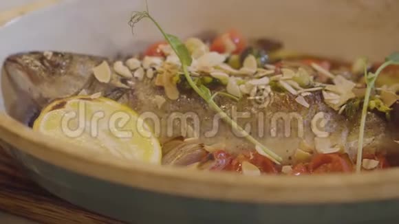 将新鲜烤鱼放在深盘中装饰有柠檬番茄樱桃蔬菜和坚果食物视频的预览图