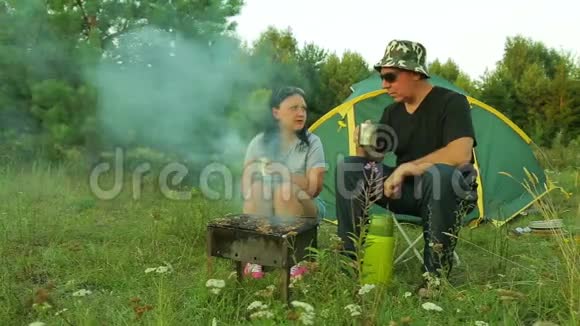 一男一女正坐在帐篷附近喝茶在烤架上煮一个什什烤肉串视频的预览图
