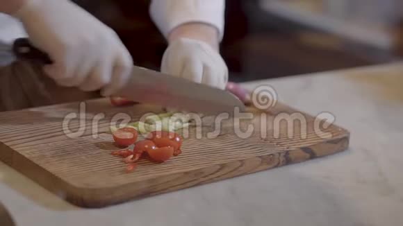 双手厨师在白色橡胶厨师手套切西红柿和绿色的木制厨房板特写慢动作视频的预览图
