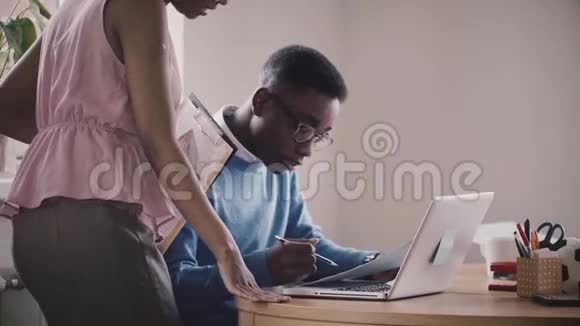 非裔美国年轻商务人士在桌子旁合作看着笔记本电脑在现代办公室慢动作特写视频的预览图