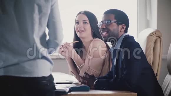 快乐的多民族团队听着无法辨认的男性高管微笑着在办公室会议上慢动作特写视频的预览图