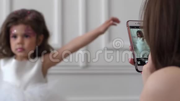 女人手里的安卓系统她把小女孩的照片做成白色的室内礼服视频的预览图