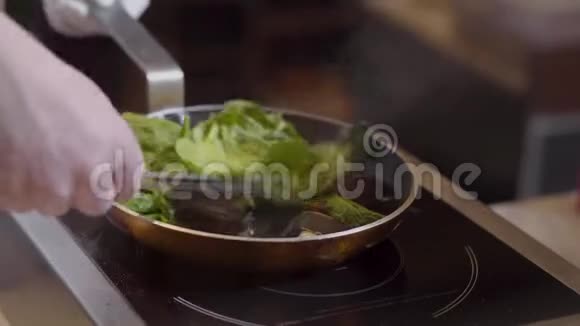 厨师用钳子将贻贝和叶子混合在嘶嘶的煎锅上用油和大蒜混合准备工作视频的预览图
