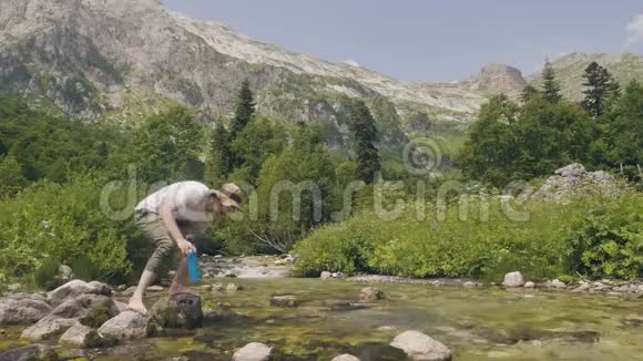 夏天旅行时徒步旅行者从山涧里拿一瓶水视频的预览图