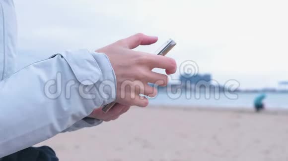 特写的女人她的手在海上背景的电话里打字海上冬天穿白色夹克的女人视频的预览图