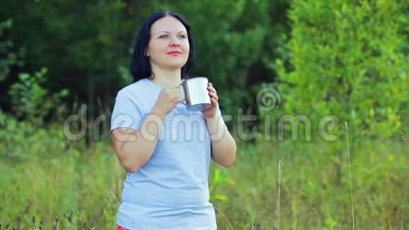 一个年轻的女人站在森林的边缘喝茶享受自己视频的预览图