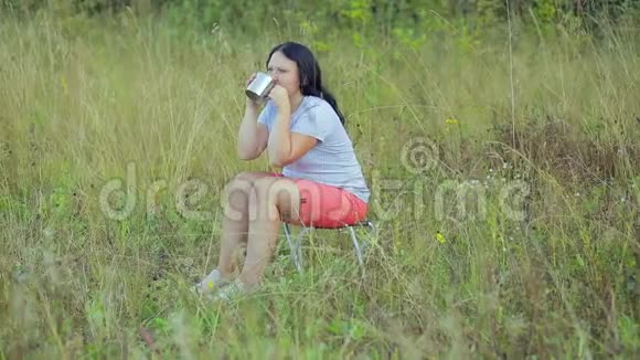 年轻女子坐在林间空地上喝茶享受视频的预览图