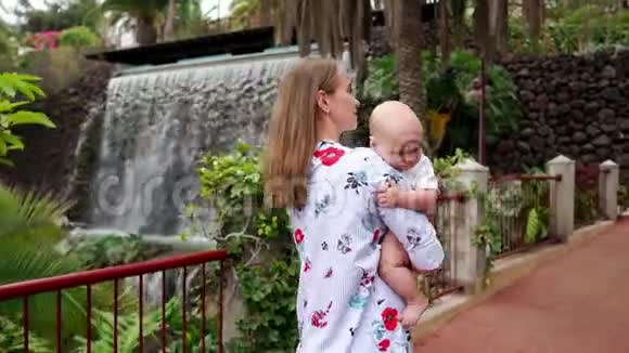 妈妈抱着宝宝在去加那利群岛旅行时沿着瀑布散步家庭度假Stadicam视频的预览图