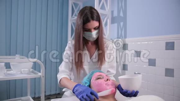 护士医生给女性做面部按摩用刷子做粉色面膜视频的预览图