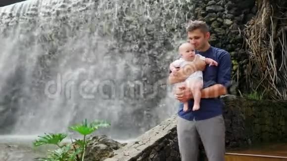 父亲带着孩子微笑拥抱婴儿的儿子关于瀑布亲吻和交谈视频的预览图