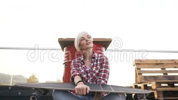日落时分美丽的时髦女孩带着滑板坐在地板上时尚生活方式一个嬉皮士的肖像视频的预览图