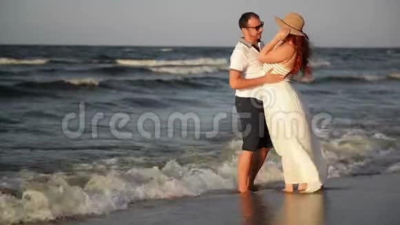 在海滩上相爱的年轻夫妇穿着白色衣服的漂亮夫妇情侣牵手拥抱视频的预览图
