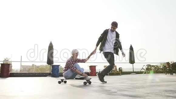 帅哥和他的女孩在现代建筑屋顶的滑板上玩得很开心一对时髦的夫妇视频的预览图