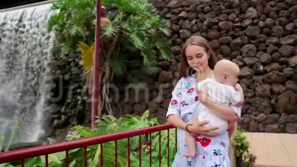 妈妈抱着宝宝在去加那利群岛旅行时沿着瀑布散步家庭度假Stadicam视频的预览图