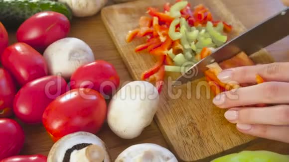 女人手在厨房桌子上的木板上用蔬菜切红和青椒视频的预览图