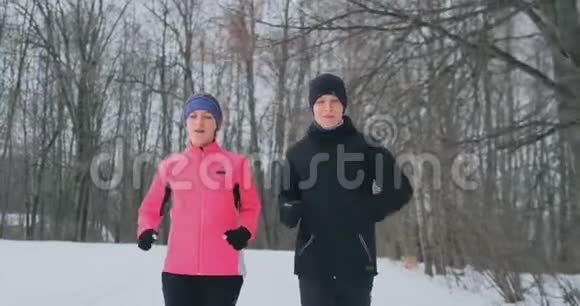 年轻的一家人在冬天的森林里晨跑穿宽松夹克的女人穿黑衣的男人视频的预览图