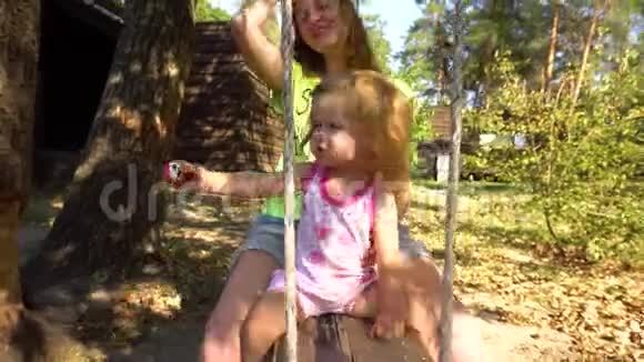 母亲和女儿坐在树下的木触发器上视频的预览图