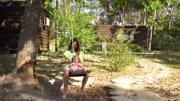 女人妈妈和女孩在树下的木跷跷板上视频的预览图