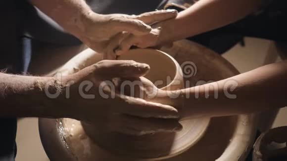 两只交织在一起的手在陶工的轮子上形成一盆粘土男人的手帮助女人他的手塑造一个粘土的形状视频的预览图