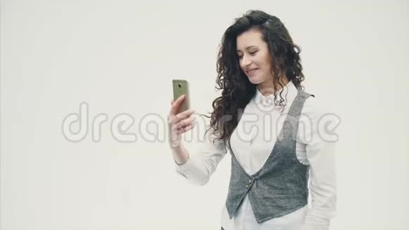 一个年轻精力充沛的卷发女孩在电话里被拍照做了一个sephi在白色背景上视频的预览图