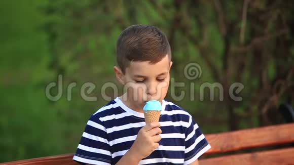 一个穿条纹T恤的小男孩正在吃蓝色冰淇淋春天晴朗的天气视频的预览图