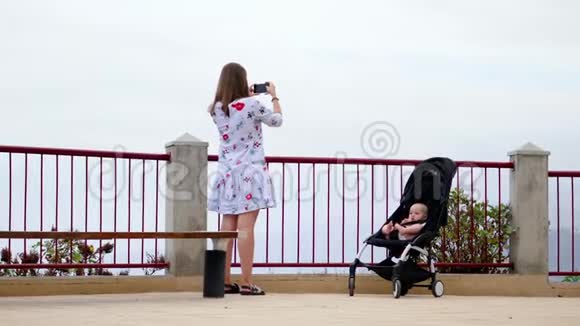 妈妈带着一个坐在轮椅上的婴儿在观察甲板上拍摄美丽的风景回忆旅程视频的预览图