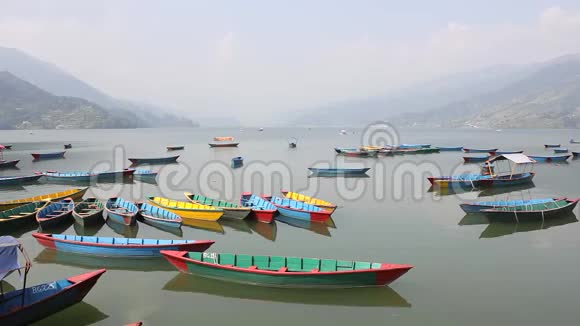 雾蒙蒙的山谷背景下的白瓦湖上空着多色木船视频的预览图