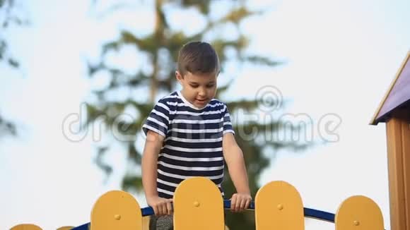 一个穿着条纹T恤的小男孩正在操场上玩在秋千上荡秋千春天晴朗的天气视频的预览图