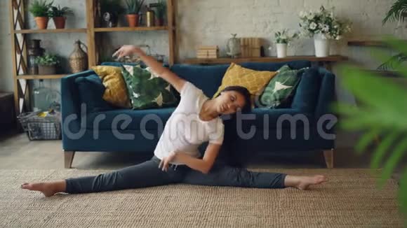 苗条的亚洲女士在家里做运动伸展身体手臂和腿坐在地板上享受活动视频的预览图