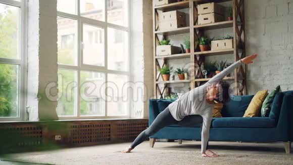 灵活的年轻女性在家锻炼在现代公寓的地板上练习瑜伽体式伸展身体手臂和身体视频的预览图
