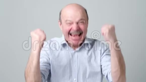 快乐的秃顶老人穿着衬衫庆祝他在灰色背景下的成功视频的预览图
