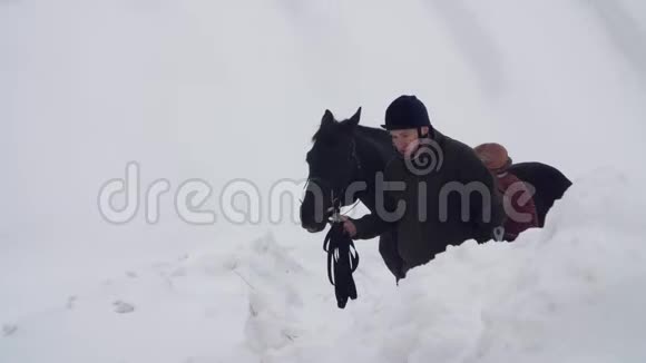 白雪皑皑的冬天残疾人骑师领路牵着一匹黑马在路上男人有假肢而不是视频的预览图
