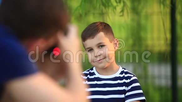 一个穿着条纹T恤的小男孩正在微笑和欢呼摄影师在拍照春天晴朗的天气视频的预览图