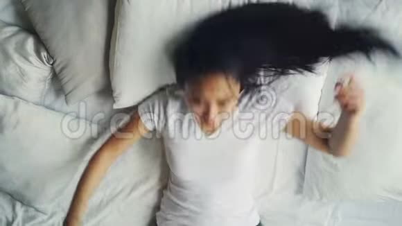 穿着休闲服装的亚洲女人躺在舒适的床上铺着白色床单抚摸着她的头发视频的预览图