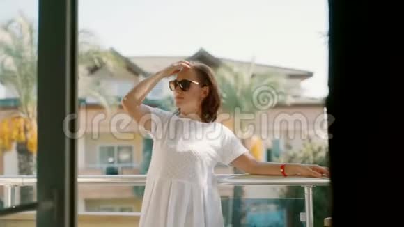 一个穿着白色连衣裙的女人站在阳台上挺直了头发视频的预览图