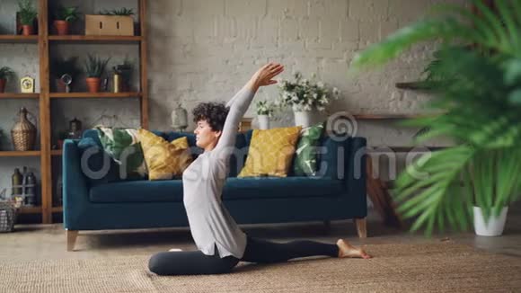 有魅力的年轻女人在家里单独练习时正在伸展腿和手臂坐在地板上健康视频的预览图