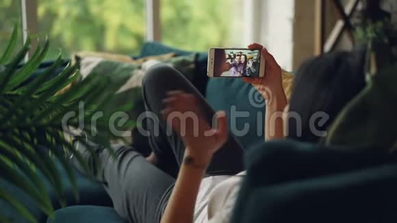 黑头发女士躺在家里的沙发上打着视频电话与朋友交流可爱的一对视频的预览图