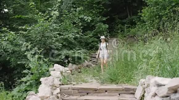 女游客在公园里散步一个戴着白色帽子的女孩拿出一部智能手机坐在公园的台阶上视频的预览图