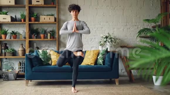 漂亮女孩专注于瑜伽练习在家里做平衡练习站在地板上一条腿健康视频的预览图