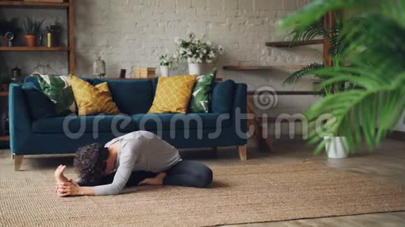 灵活的女孩弯着腰坐在座位上扭动身体享受瑜伽和活动坐在地板上视频的预览图