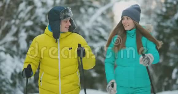 微笑的男人穿着冬季夹克在树林里缓慢地和他可爱的妻子一起滑雪健康的生活方式年轻夫妇视频的预览图